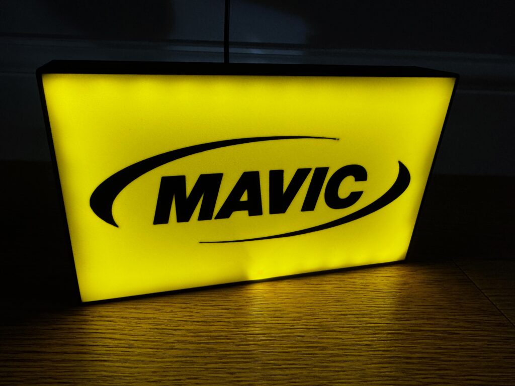 Yellow illuminated MAVIC sign with black logo on wooden floor