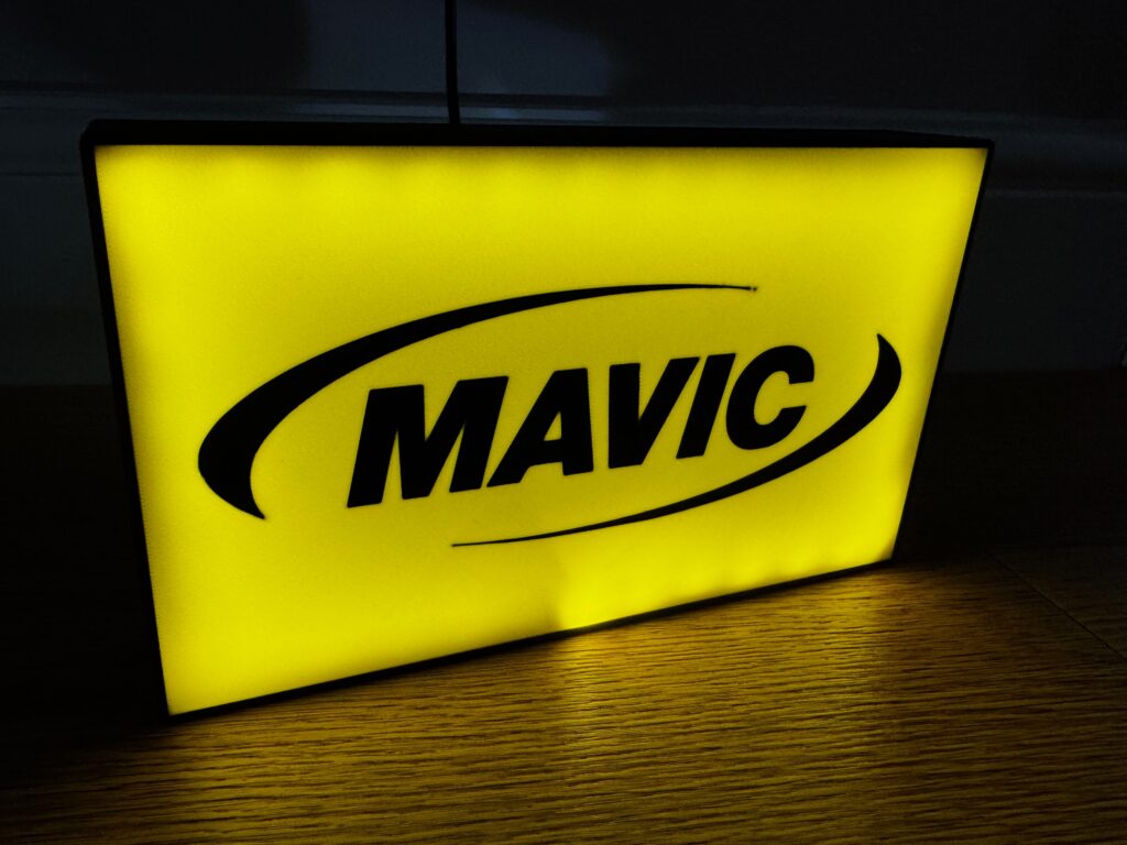 Yellow illuminated MAVIC sign with black logo on wooden floor