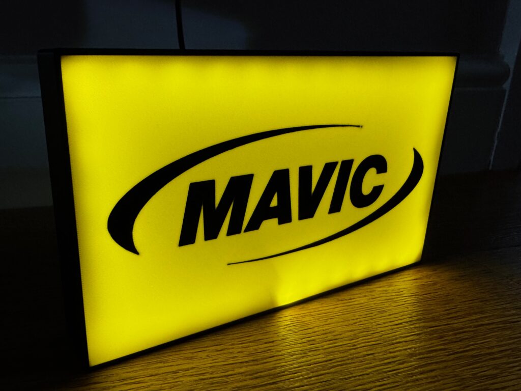 Yellow illuminated MAVIC sign with black logo on wooden floor