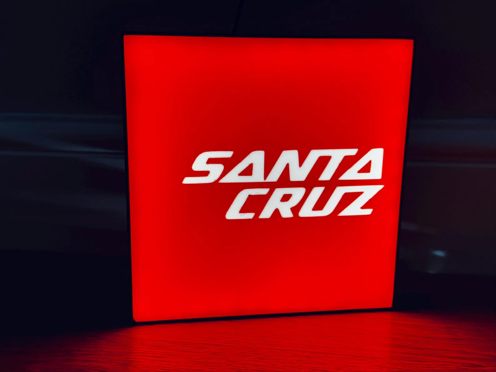 Illuminated Santa Cruz light box glowing white logo on black background